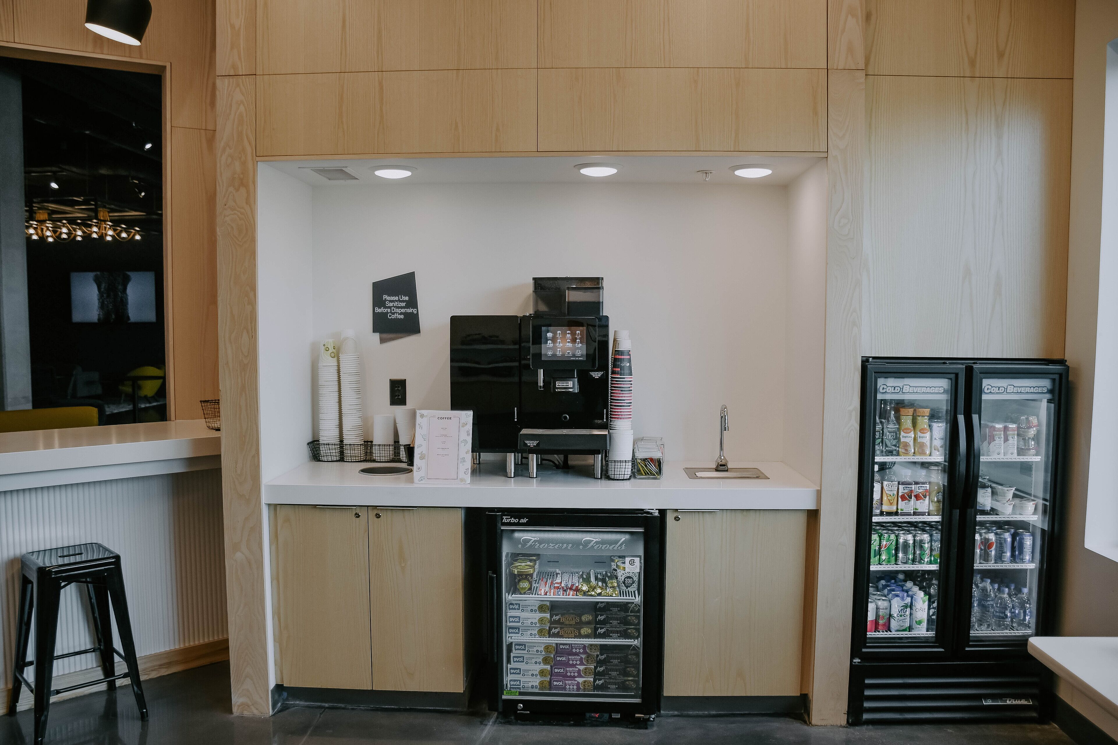 A self-service coffee station with a coffee machine, a beverage dispenser, and a refrigerator stocked with drinks.