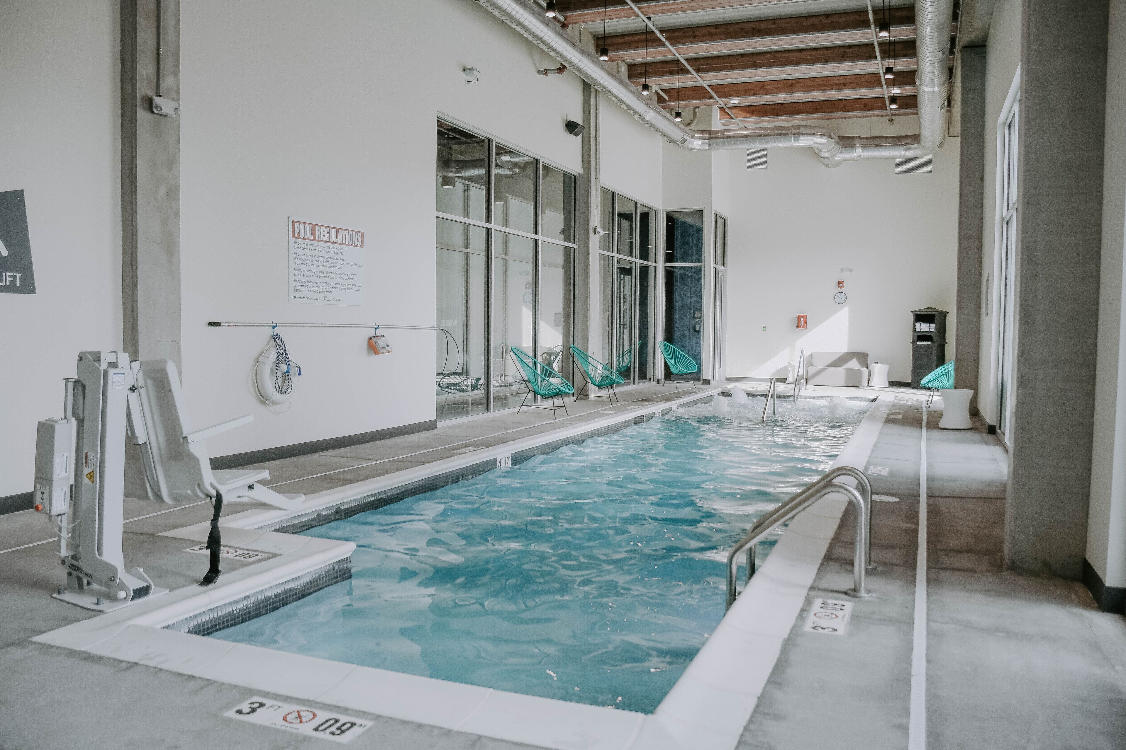 A swimming pool with clear water, surrounded by glass doors and windows, and equipped with safety railings.