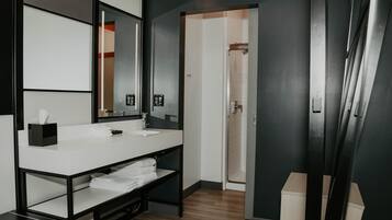 Un baño moderno con un lavamanos blanco, encimera negra y un espejo grande. Se observa un toallero con toallas dobladas y un cubo de basura negro.