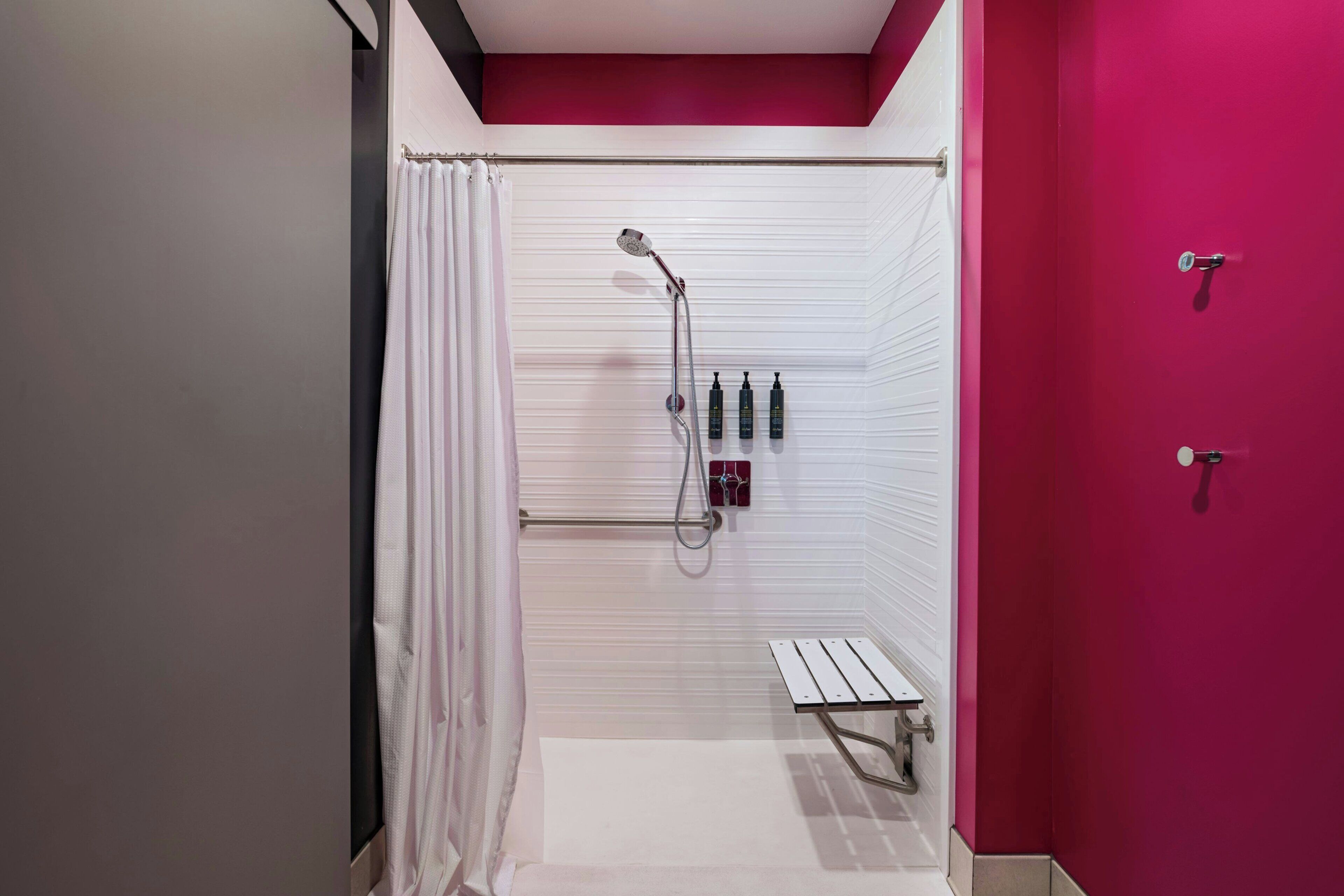 A modern bathroom with a shower, a bench, and a set of toiletries on the wall.