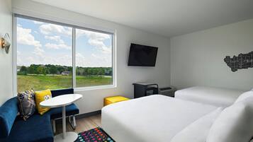 A hotel room with a large window, a bed, a sofa, a small table, and a TV mounted on the wall.