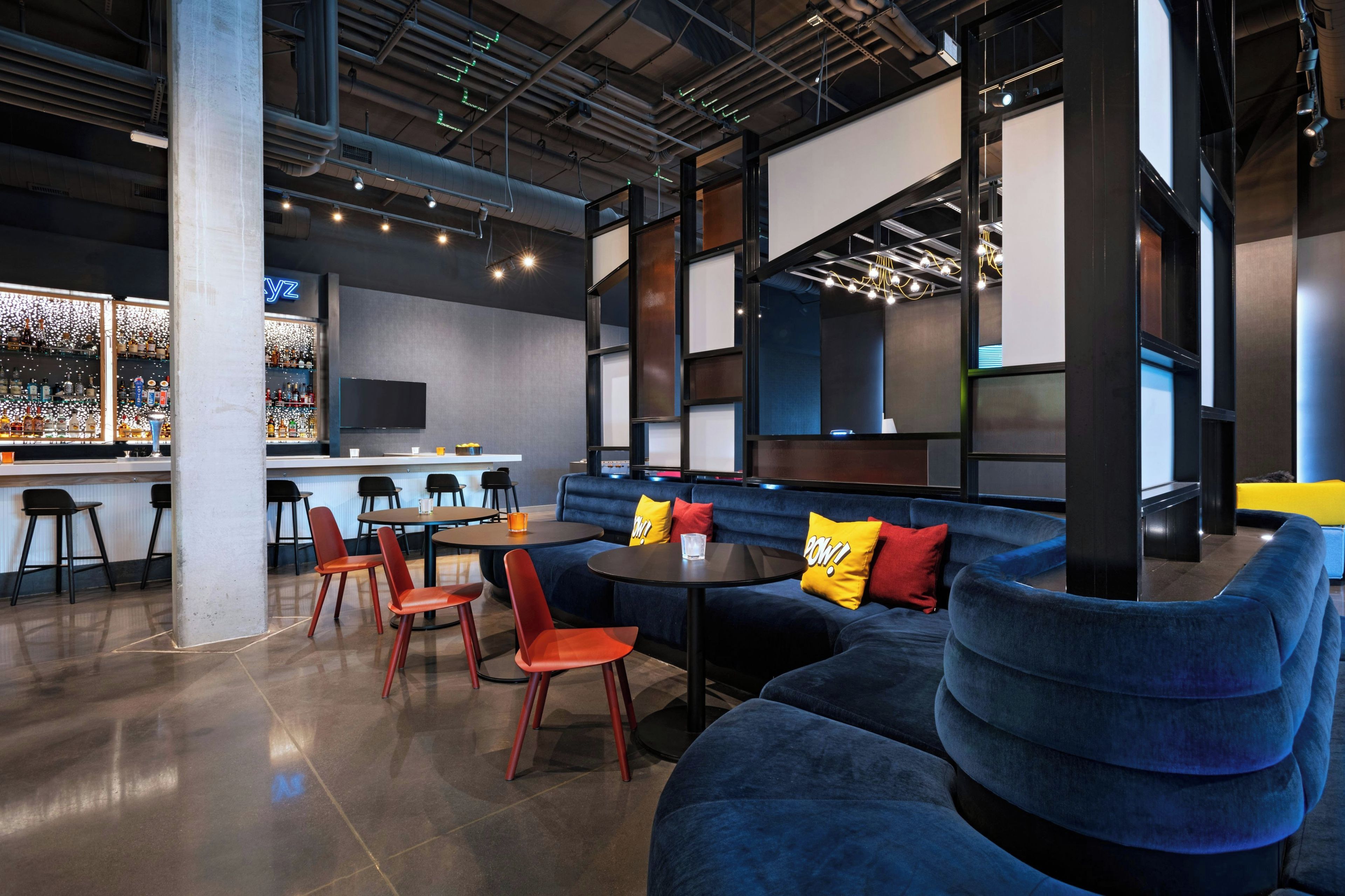 A modern lounge area with seating, a bar, and a large screen.