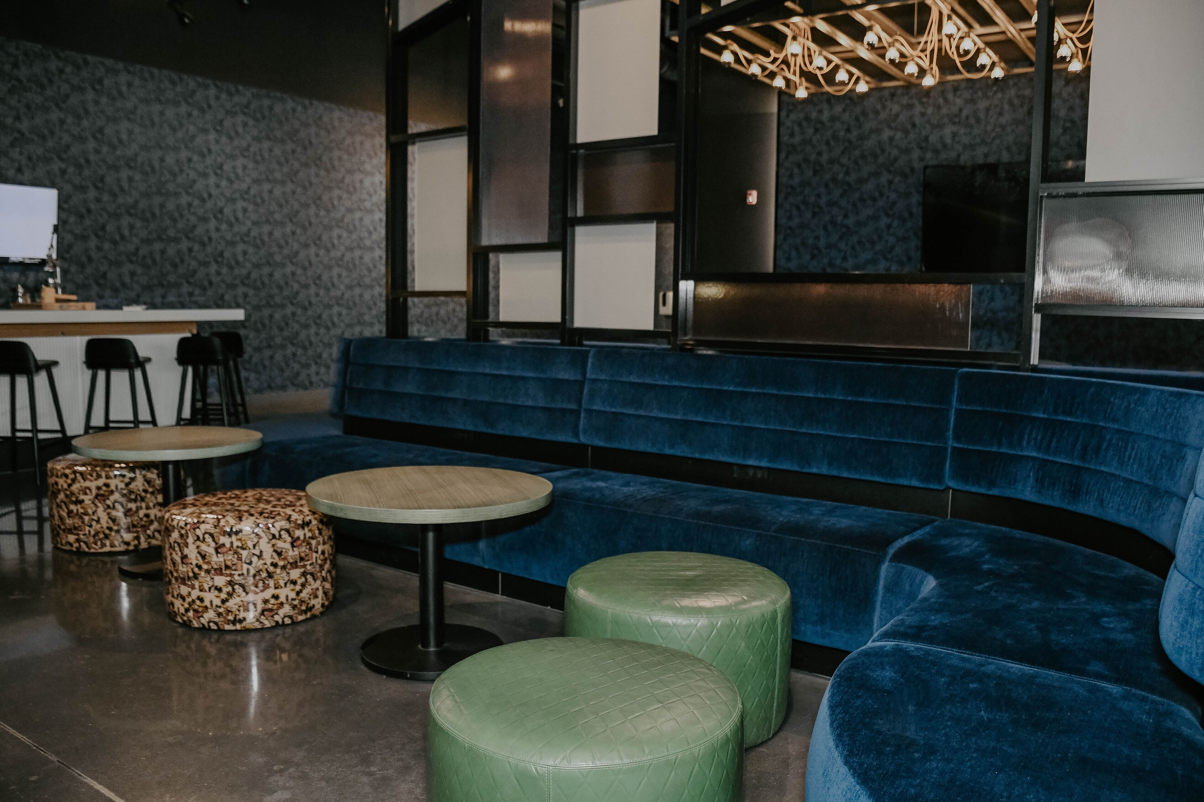 A modern lounge area with a blue sofa, green ottomans, and patterned stools.