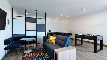 A modern living room with a sofa, a coffee table, a foosball table, and a patterned rug.