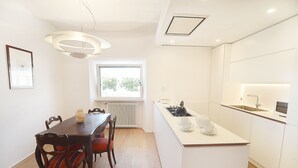 A modern kitchen with white cabinetry, a dining area with a wooden table and chairs, and a large window providing natural light. - Beautiful apartment in the center of Rome (Roma)