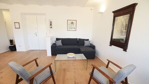 A living room with a dark-colored sofa, two wooden chairs, a glass coffee table, and a framed picture on the wall. - Beautiful apartment in the center of Rome (Roma)