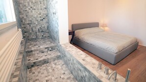A modern bedroom with a bed, nightstand, and a small bathroom area with a shower. - Beautiful apartment in the center of Rome (Roma)