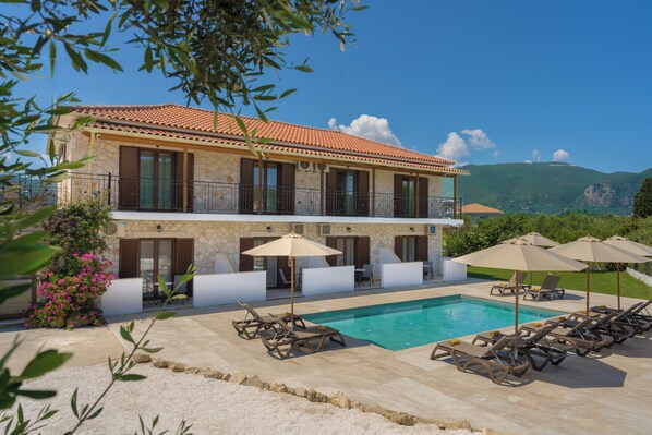 A two-story building with a swimming pool, outdoor seating, and a view of mountains.
