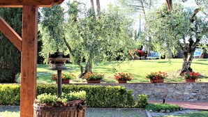 Una pergola in legno con un alimentatore per uccelli rustico, circondata da un muro in pietra e vasi con fiori rossi.