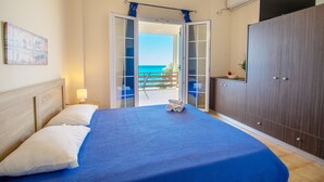 Un dormitorio con cama, mesita de noche, armario y vista al mar.