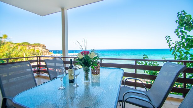 Una mesa de vidrio con sillas en un balcón con vista al mar.
