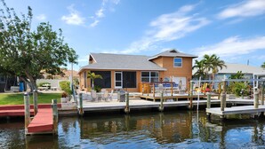 A waterfront property with a dock, outdoor seating, and a house with a large window overlooking the water. - Beautiful Matlacha Isles direct access waterfront home with dock, lift and deck (Matlacha)