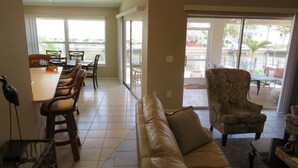 A spacious living area with a sofa, dining table, and chairs. A ceiling fan is visible, and there is a sliding glass door leading to an outdoor patio. - Beautiful Matlacha Isles direct access waterfront home with dock, lift and deck (Matlacha)