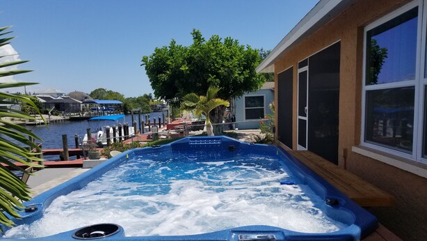 A hot tub with a wooden frame, a view of a marina with boats, and a building with large windows. - Beautiful Matlacha Isles direct access waterfront home with dock, lift and deck (Matlacha)