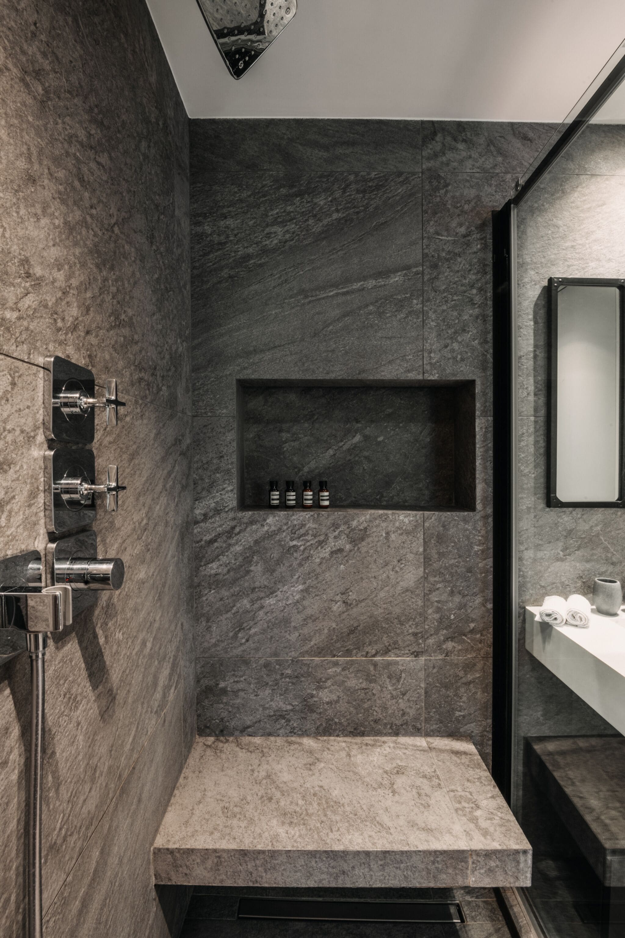 A modern bathroom with a built-in shower, a marble wall, and a shelf with toiletries.