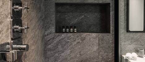 A modern bathroom with a built-in shower, a marble wall, and a shelf with toiletries.