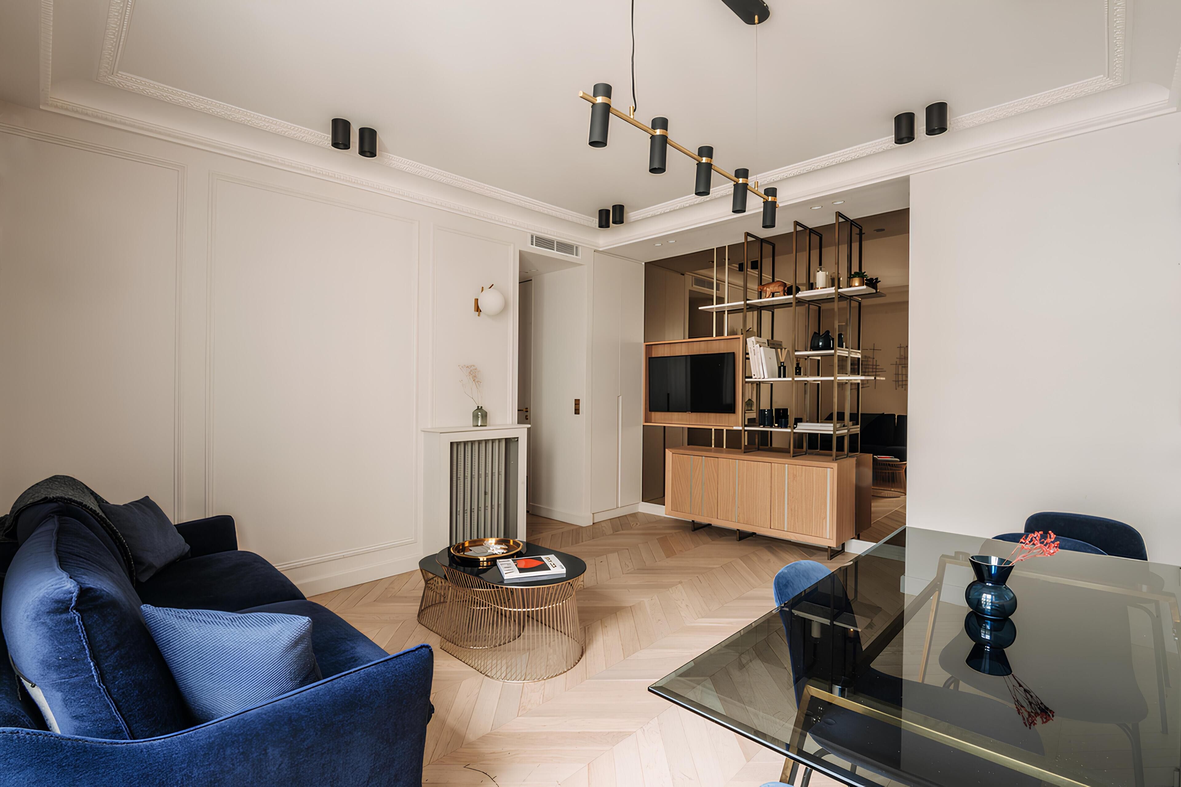 Ein modernes Wohnzimmer mit einem Glastisch, einem blauen Sofa und einem Essbereich mit einem Glastisch und Stühlen.