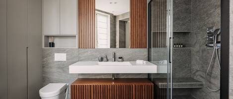 A modern bathroom with a glass-enclosed shower, a white sink, and a wooden bench.
