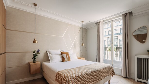 A modern bedroom with a large bed, wooden headboard, bedside tables, a mirror, and a window with curtains. -  HIGHSTAY - Luxury Serviced Apartments - Rue de Rivoli (Paris)