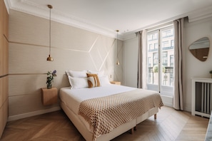 Een moderne slaapkamer met een groot bed, een houten hoofdbord, nachtkastjes, een spiegel en een raam met gordijnen.
