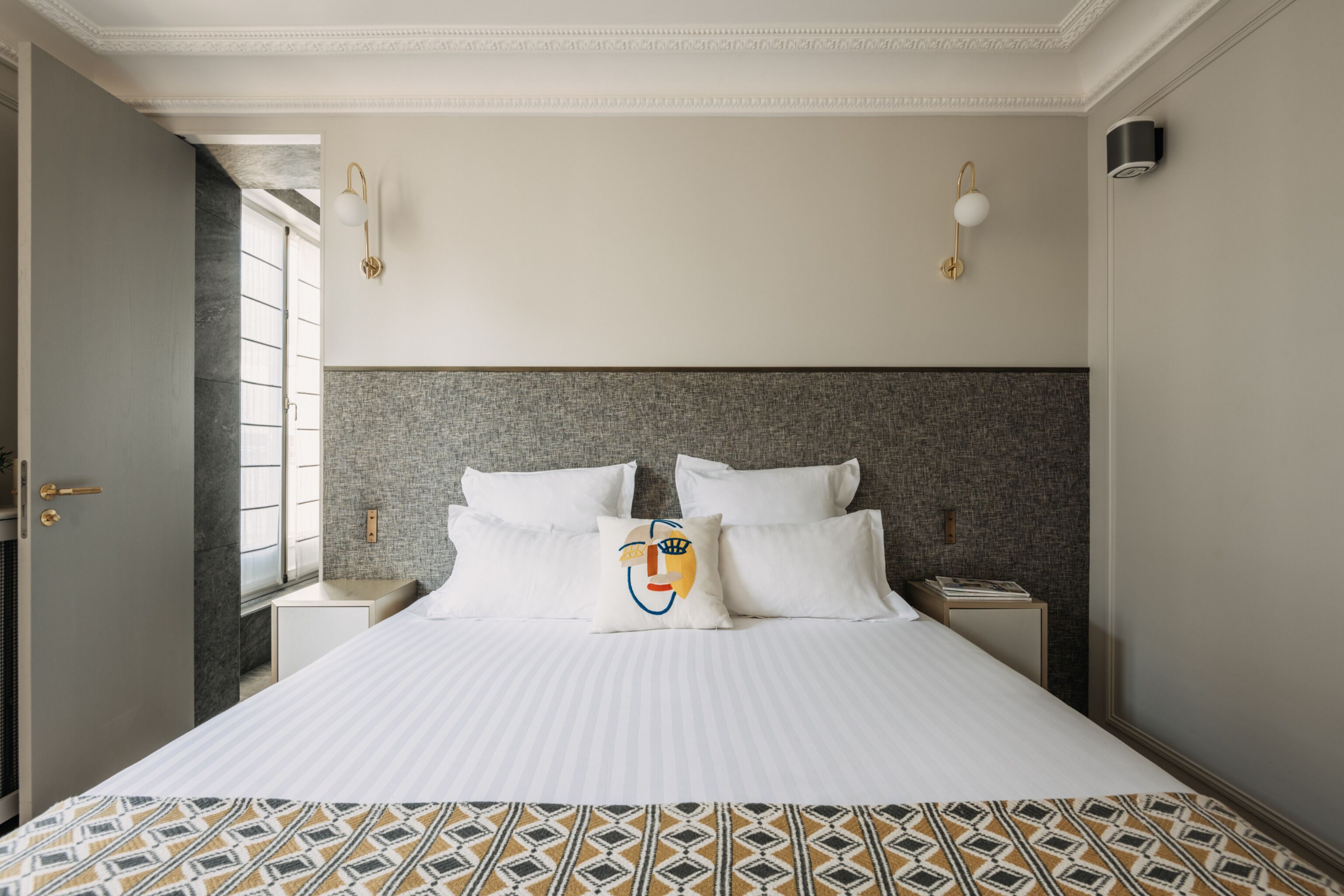 A neatly made bed with a patterned bedspread, a headboard with a textured design, and two bedside lamps.
