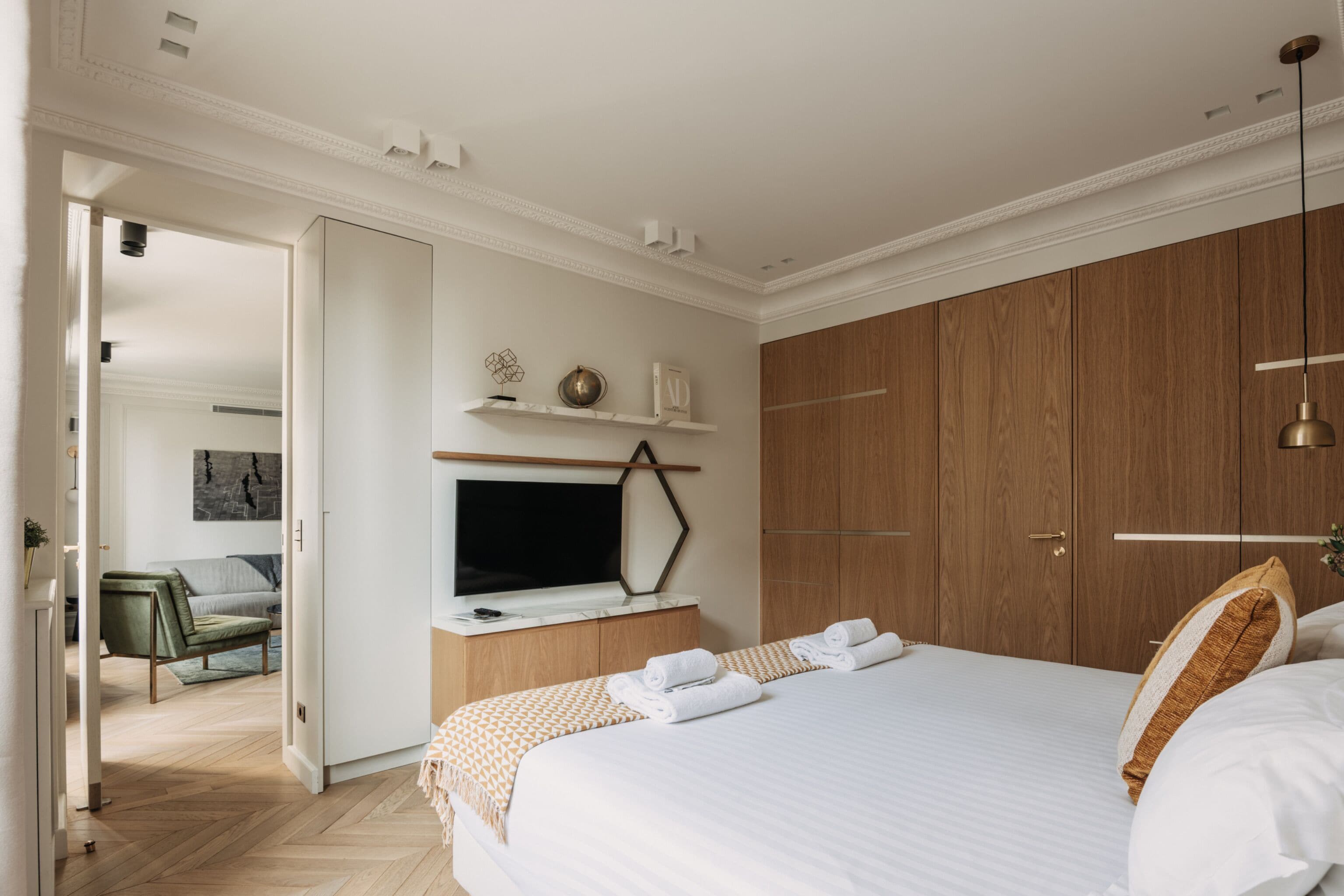 A hotel room with a large bed, wooden wardrobe, a TV on a wooden stand, and a view of the hallway.