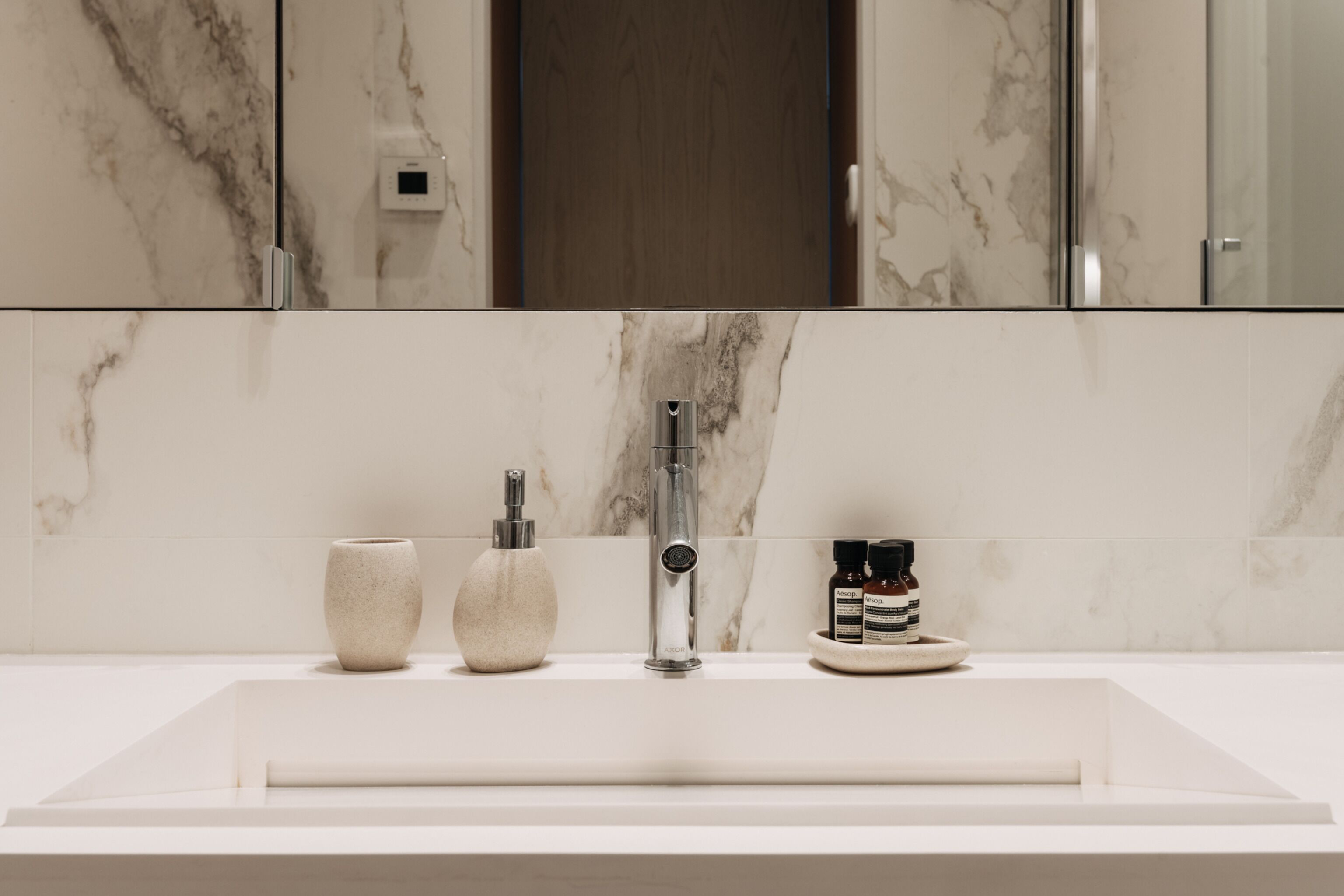 Une salle de bain moderne avec un lavabo en marbre, un robinet, un distributeur de savon et deux bouteilles de shampoing.