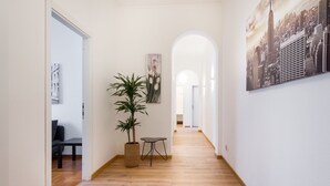 A hallway with wooden flooring, a potted plant, a small table, and a cityscape painting on the wall. - AT THE HOME OF PABLO COMO (Como)