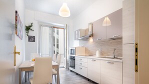 A modern kitchen with white cabinetry, a dining area with a table and chairs, and a large window providing natural light. - AT THE HOME OF PABLO COMO (Como)