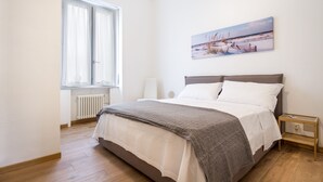 A bedroom with a bed, a window, a radiator, a bedside table, and a wall-mounted picture. - AT THE HOME OF PABLO COMO (Como)
