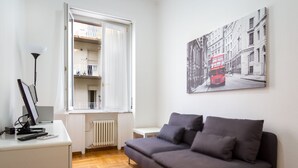 A modern living room with a grey sofa, a white desk with a computer, a lamp, and a window with a view of a balcony. - AT THE HOME OF PABLO COMO (Como)