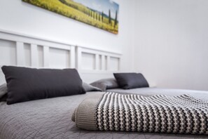 A neatly made bed with a patterned blanket and two pillows, a white headboard, and a painting on the wall.