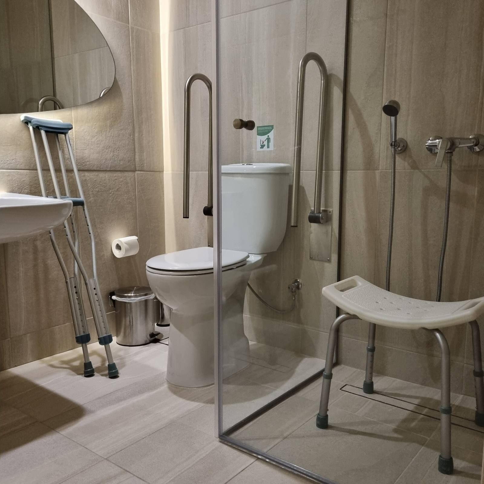 Une salle de bain moderne équipée de toilettes, d’un bidet et d’un siège de douche accessible aux personnes en fauteuil roulant.