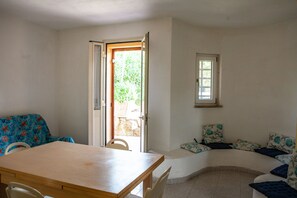 A room with a wooden table, a curved sofa with patterned cushions, and a door leading to an outdoor area. - FANTASTICO PORTO OTTIOLU (Budoni)