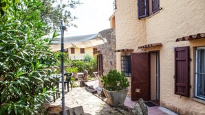 A courtyard with stone flooring, potted plants, outdoor furniture, and a building with wooden shutters. - FANTASTICO PORTO OTTIOLU (Budoni)