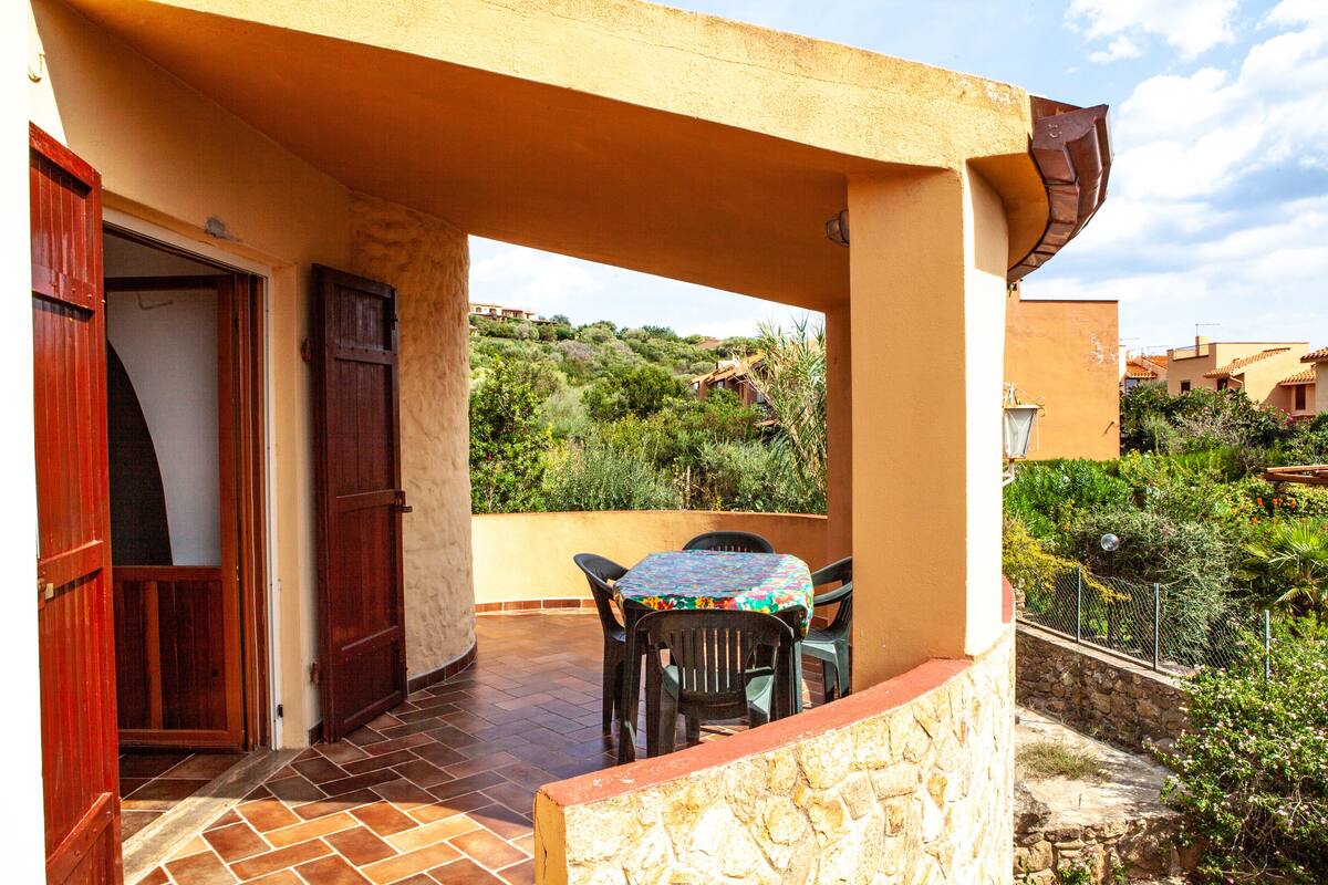 An outdoor patio with a table and chairs, a stone wall, and a view of a hillside with vegetation.