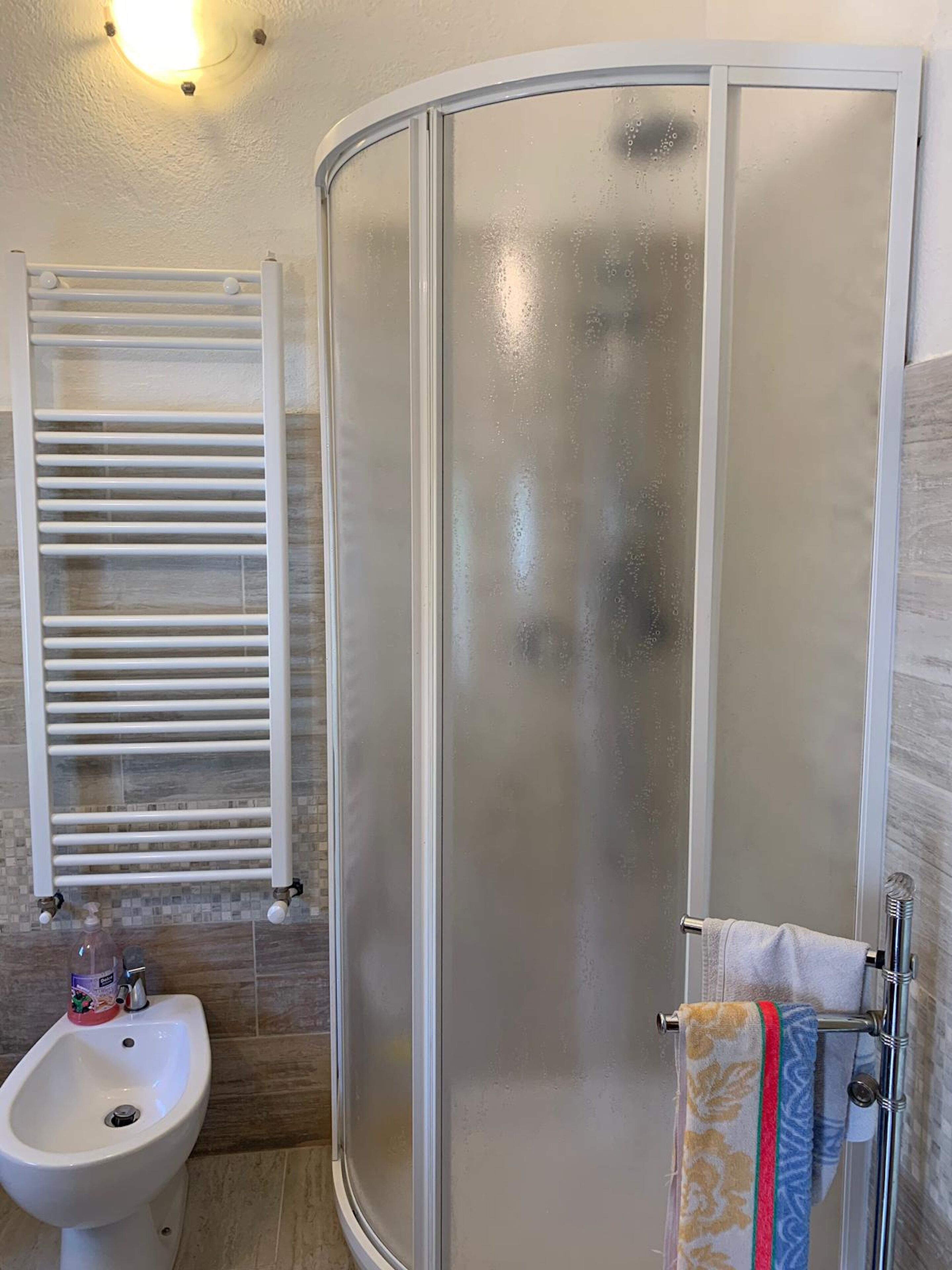 Ein Badezimmer mit einer gläsernen Duschkabine, einem weißen Waschbecken und einem Handtuchhalter mit mehreren Handtüchern.
