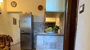 Eine Küche mit Kühlschrank, Spüle und einer Arbeitsfläche mit Früchten. Auf dem Boden liegt ein Teppich mit Muster.