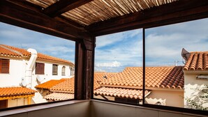 A balcony with a view of terracotta-roofed buildings, a round table, and a wooden ceiling structure. - FANTASTICO PORTO OTTIOLU GR1 (Budoni)