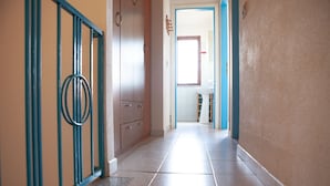 A hallway with a tiled floor, a door with a blue frame, and a wall-mounted light fixture. - FANTASTICO PORTO OTTIOLU GR4 (Budoni)