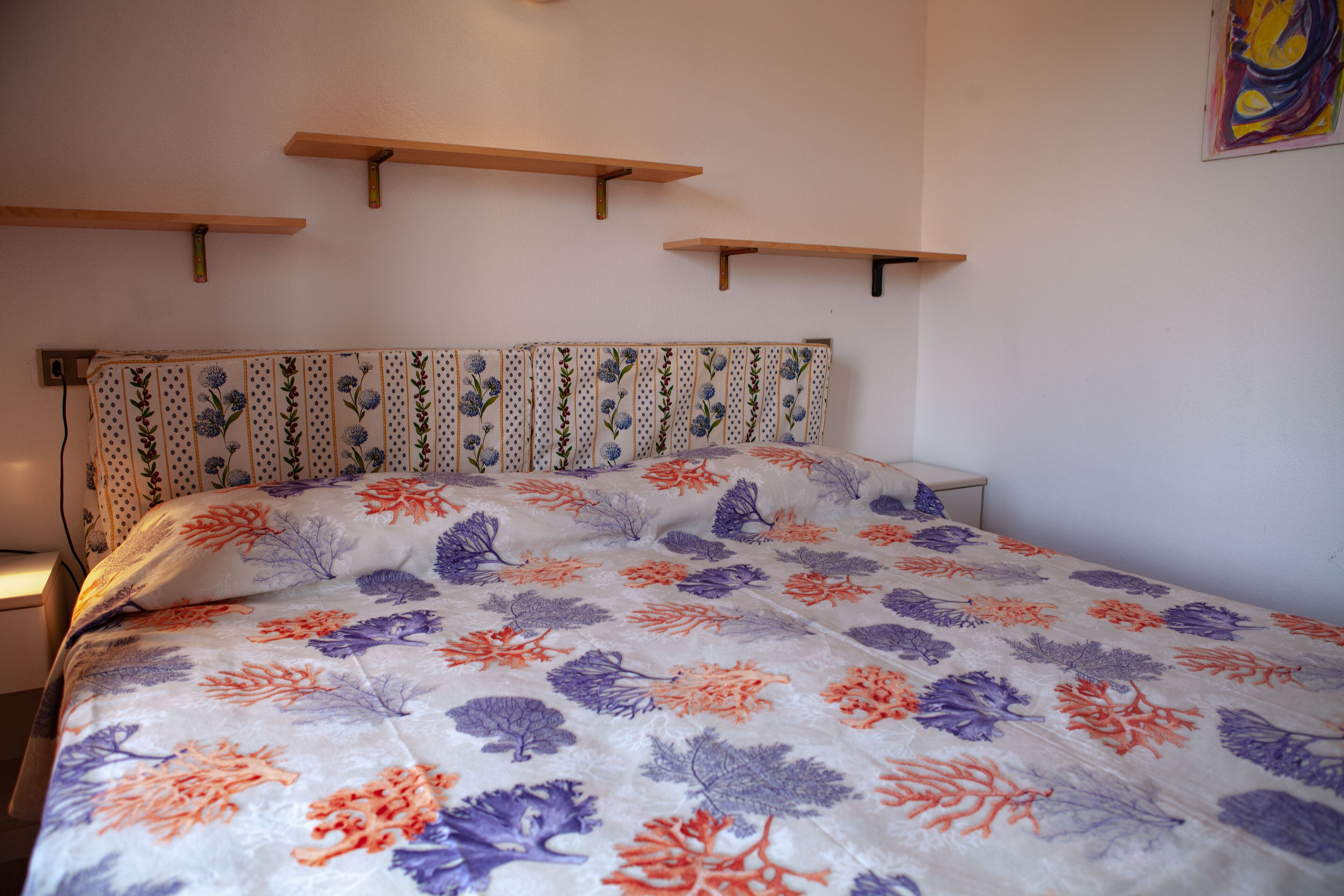 Een slaapkamer met een bloemenbedekker, houten hoofdbord en nachtkastjes.