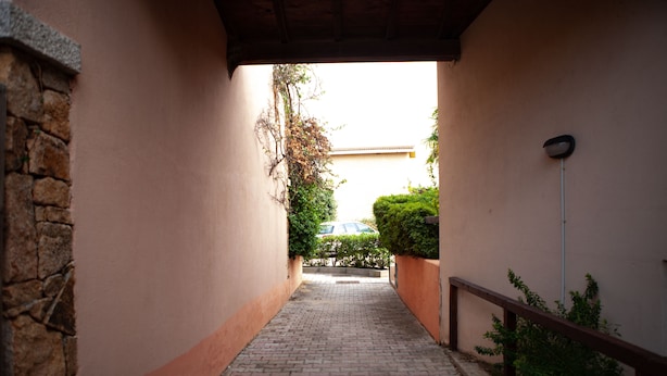 A narrow brick pathway leading to a building entrance with a stone wall on one side and a wooden railing on the other. - FANTASTICO PORTO OTTIOLU GR4 (Budoni)