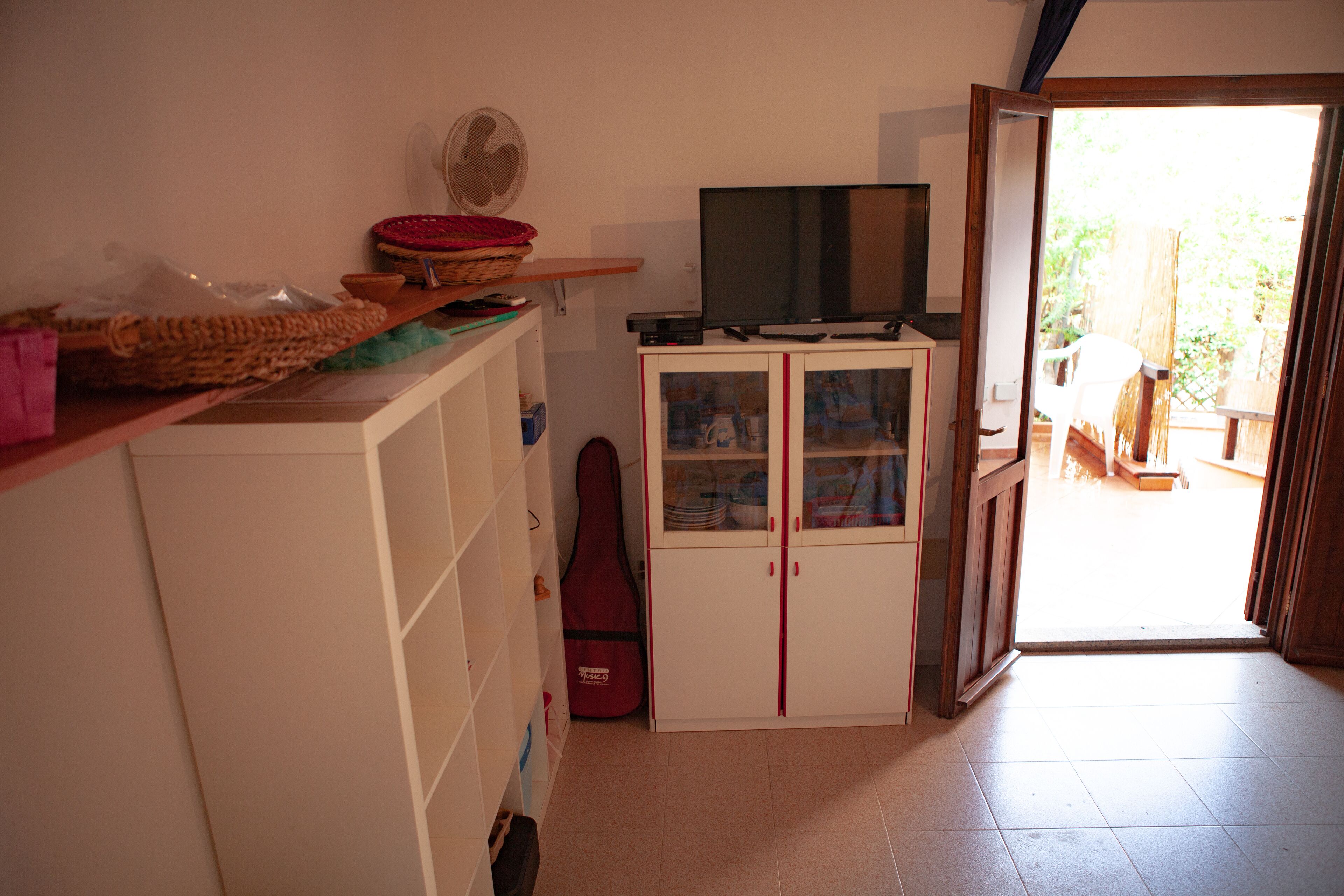 A room with a TV on a cabinet, a guitar, and a fan on the wall.