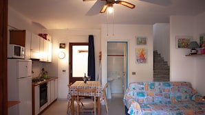 A compact kitchen with a dining table and chairs, a bed with a colorful cover, a ceiling fan, and a staircase leading to another room. - FANTASTICO PORTO OTTIOLU GR4 (Budoni)