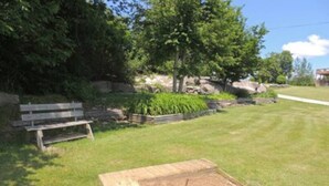 A grassy area with a wooden structure, a bench, and a pathway. - Cottage #6 - 2 bedroom/ 1 bath (Cape Vincent)