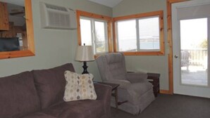 A room with a brown sofa, a grey armchair, a lamp, and a door leading to an outdoor area. - Cottage #6 - 2 bedroom/ 1 bath (Cape Vincent)