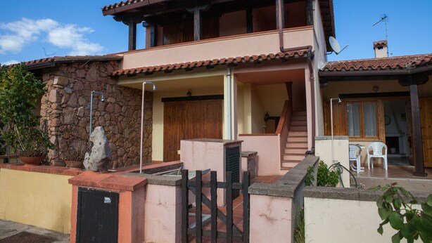 A two-story house with a stone facade, a wooden balcony, and a tiled roof. - FANTASTICO SAN TEODORO FS-AH01 (San Teodoro)