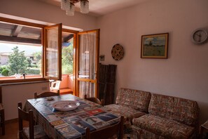 A dining area with a table set for two, a sofa, and a window with curtains. - FANTASTICO SAN TEODORO FS-AH01 (San Teodoro)