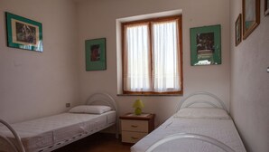 A bedroom with two single beds, a window with curtains, and a nightstand with a lamp. - FANTASTICO SAN TEODORO FS-AH01 (San Teodoro)
