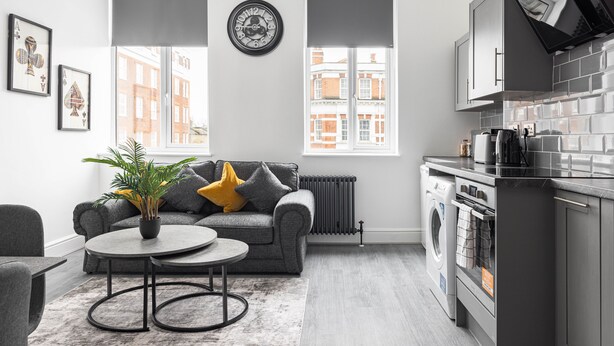 A modern kitchen with grey cabinetry, a built-in oven, and a black range hood. - Edgware Road Apartments (London)